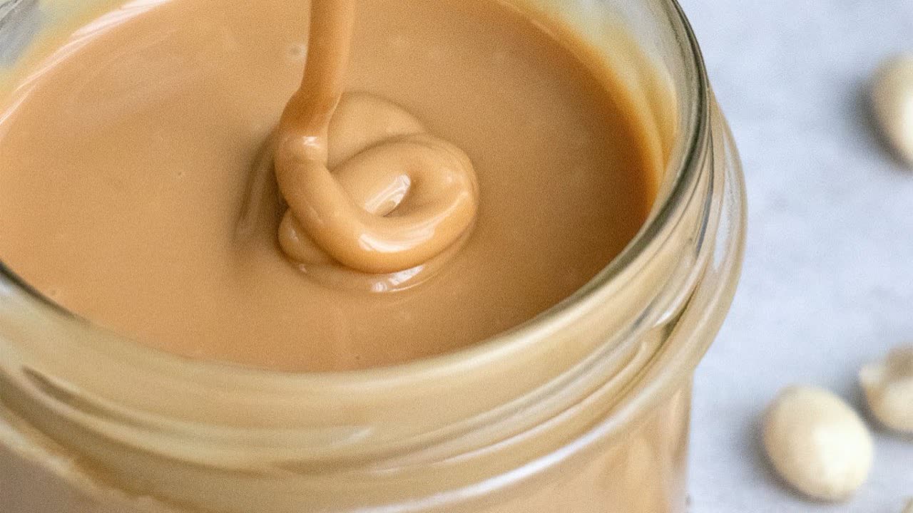 Smooth peanut butter being poured into a jar